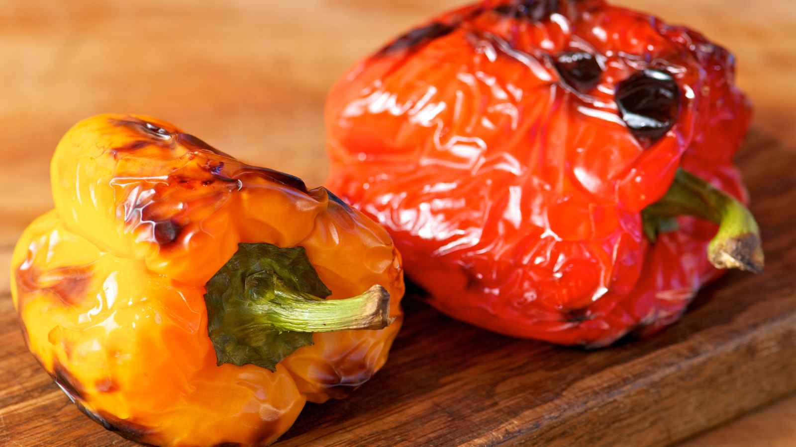 A grilled yellow and a red bell pepper on a wooden surface, showing charred skin.