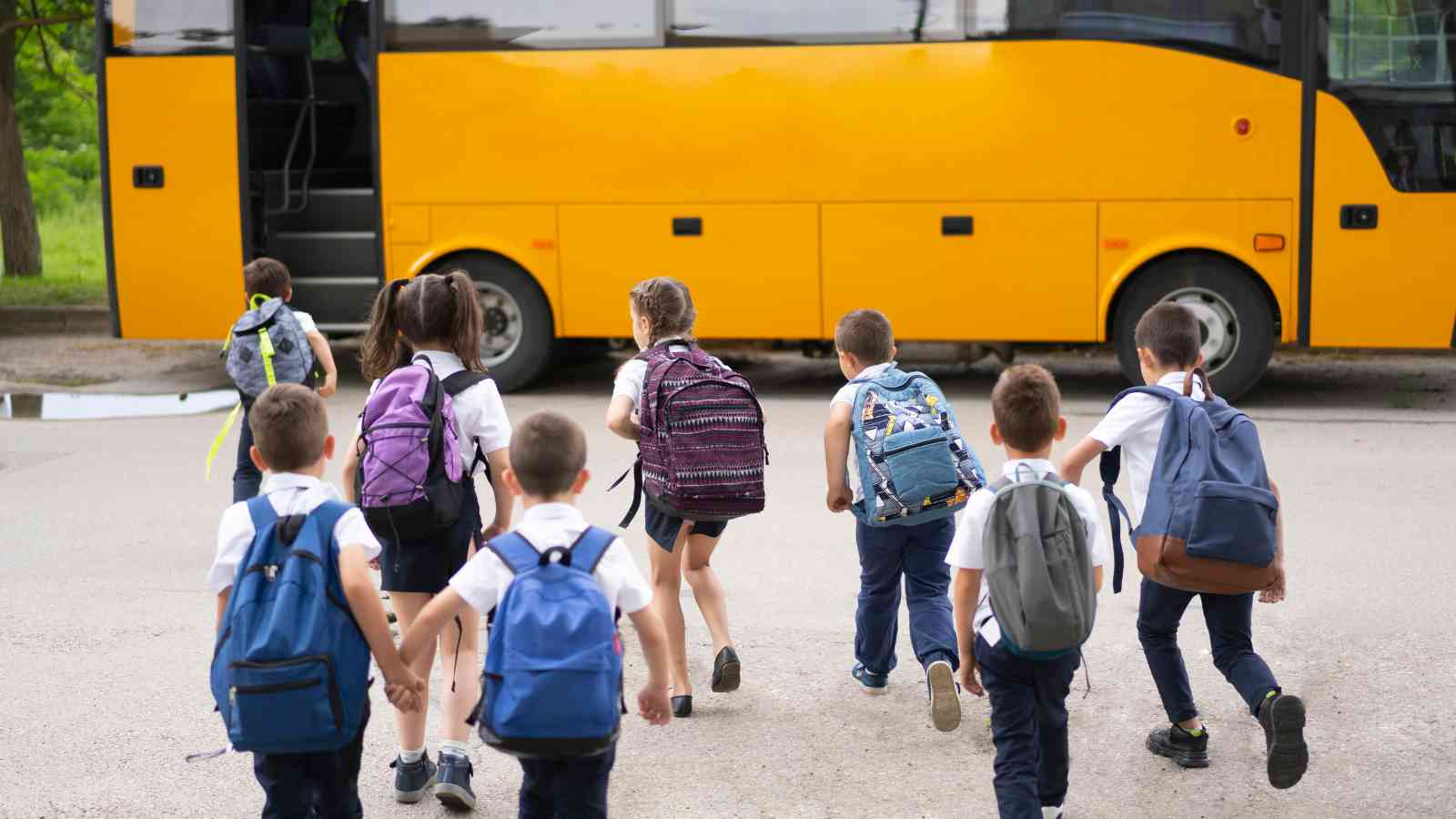A group of school children with backpacks walking toward a yellow school bus parked on the street.