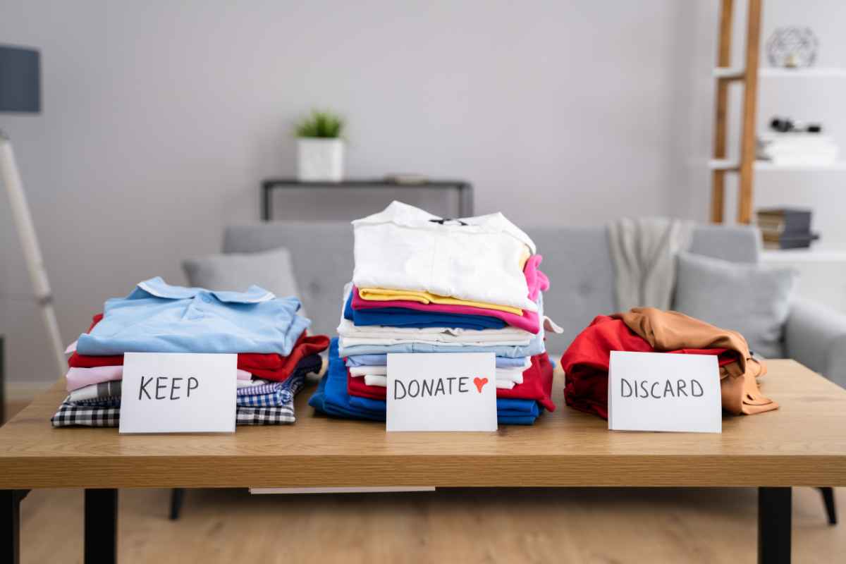 A table with three piles of folded clothes labeled "Keep," "Donate," and "Discard," set in a living room.