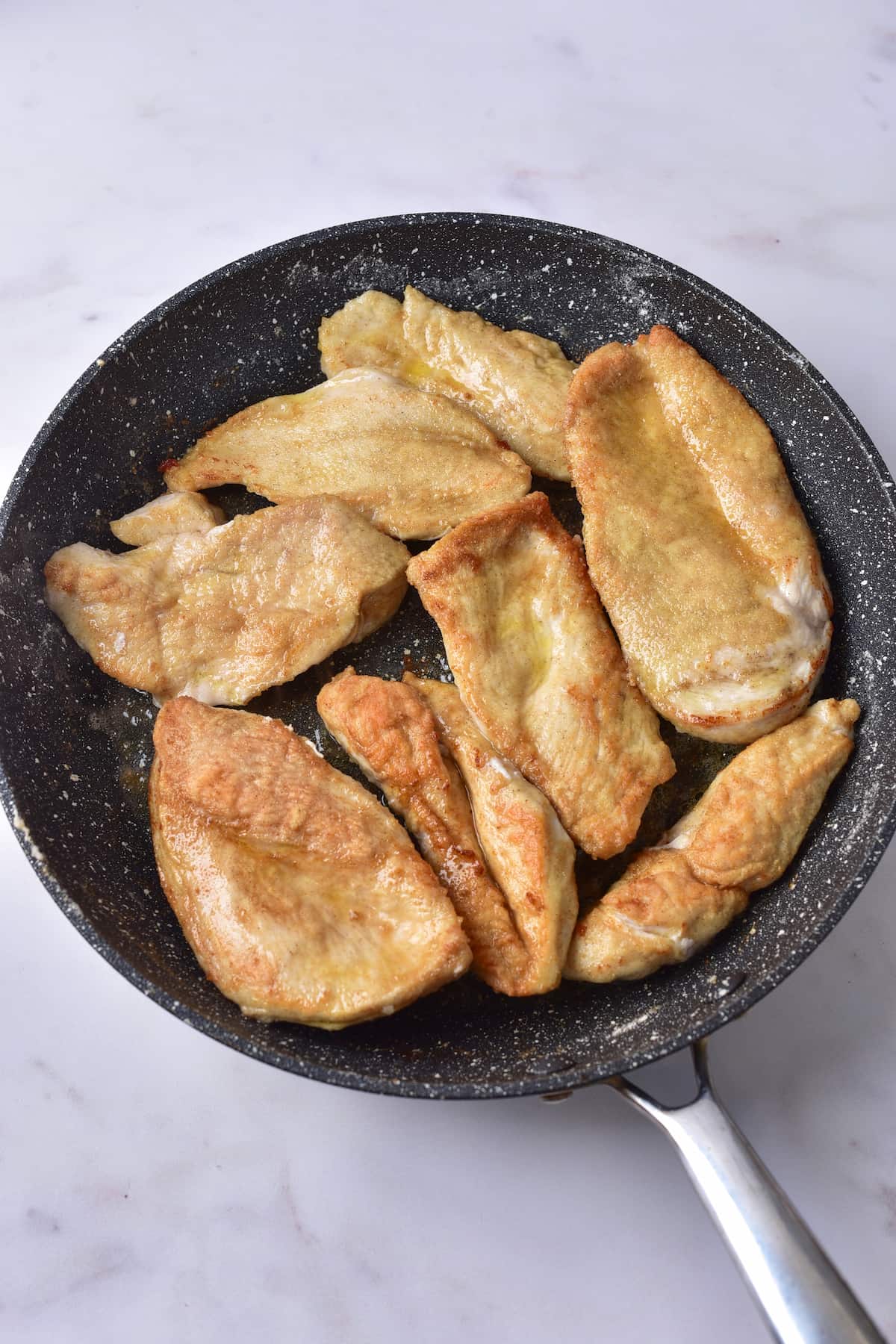 Several pieces of cooked chicken breast, reminiscent of marry me chicken, are shown in a black frying pan on a light-colored surface.