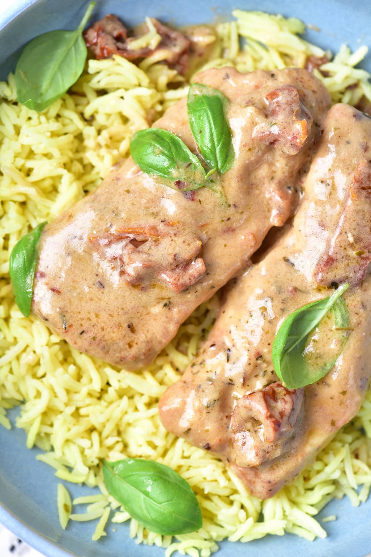 Two pieces of chicken covered in creamy sauce with herbs, served on a bed of yellow rice and garnished with fresh basil leaves.