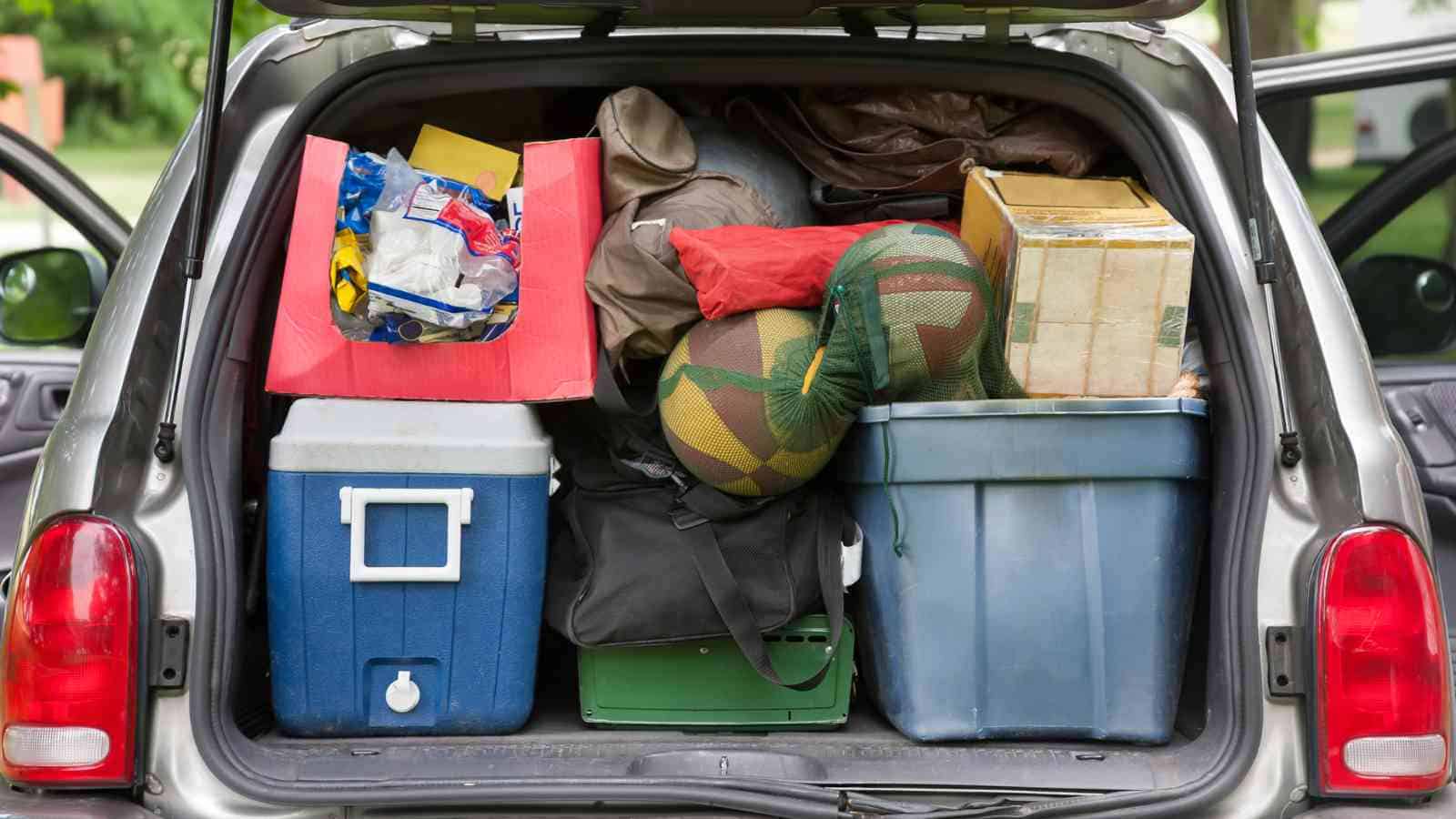SUV trunk packed with various items, including a blue cooler, plastic bins, duffel bags, boxes, and sports equipment, with both rear doors open.
