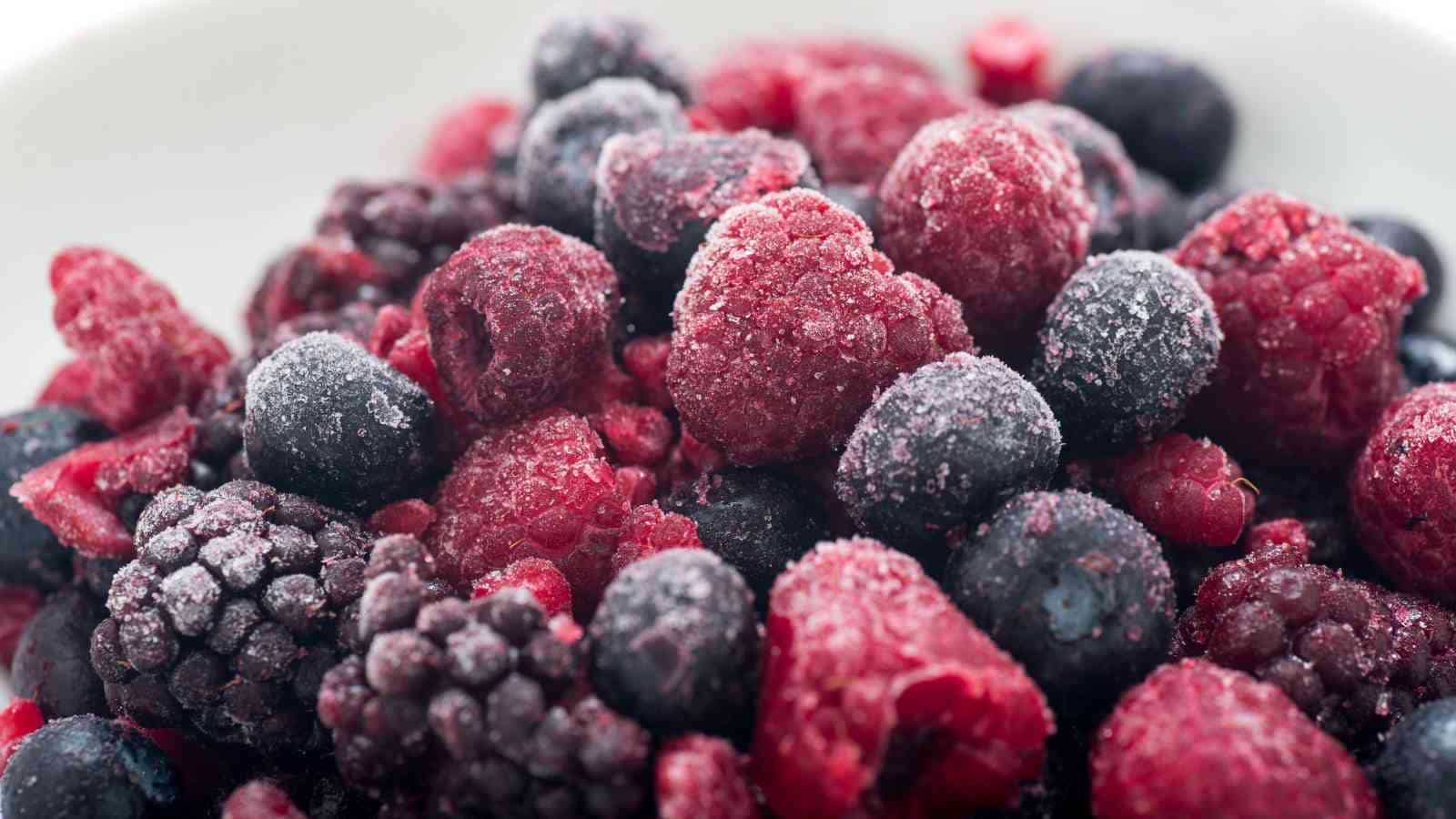 A close-up of assorted frozen berries, including raspberries, blackberries, and blueberries, covered in a layer of frost.