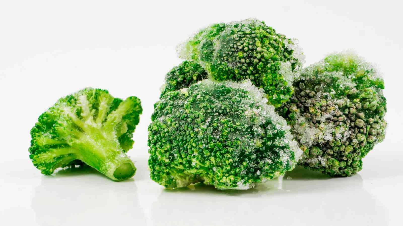 Frozen broccoli florets covered with ice crystals on a white background.