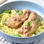 Two pieces of marry me chicken in a creamy sauce are served over yellow rice and garnished with fresh basil leaves in a blue bowl.