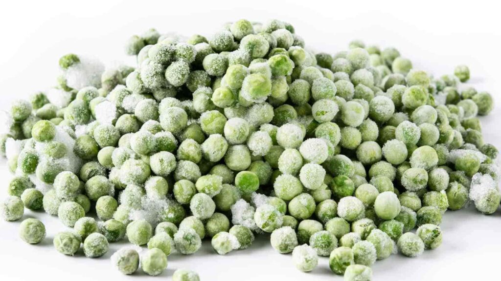 A pile of frozen green peas, lightly covered with frost, on a white background.