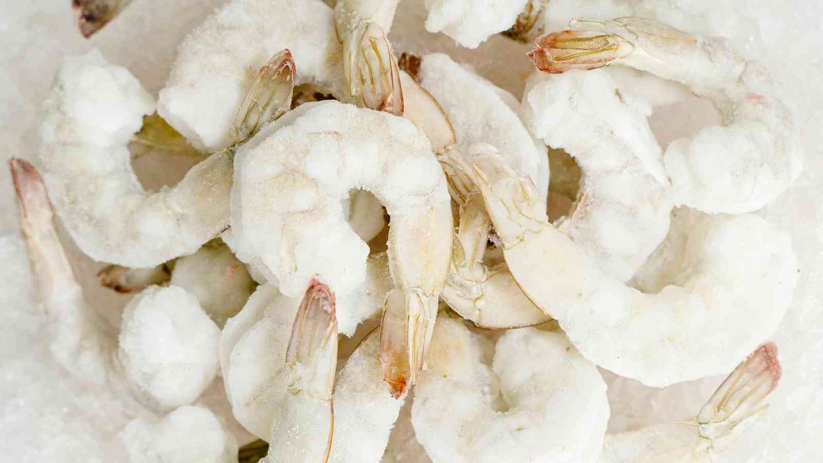 A pile of raw, frozen shrimp with tails on, covered in a layer of ice.
