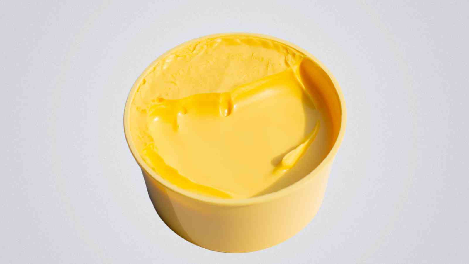 A round yellow container filled with margarine, showing a smooth surface and a scoop taken from one side.