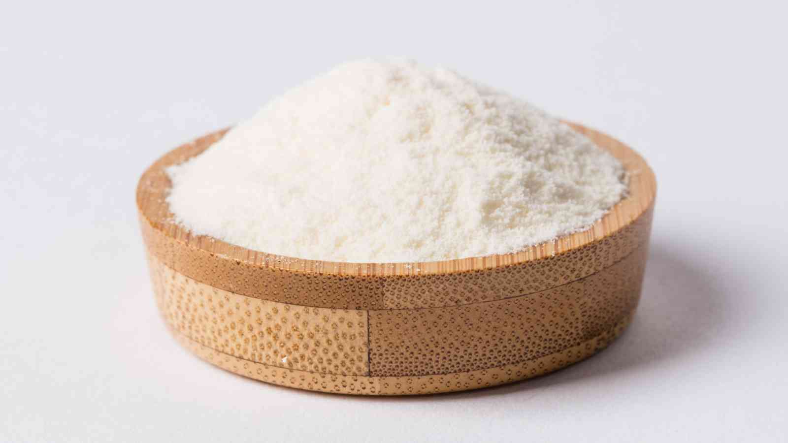 A small wooden bowl filled with a mound of fine white powder, placed on a white surface.