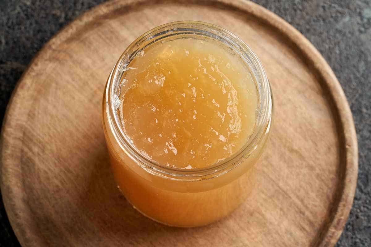 A glass jar filled with light brown, translucent jelly sits on a round wooden surface.