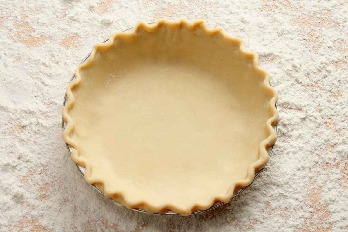 Unbaked pie crust in a fluted pie dish, set on a floured surface.