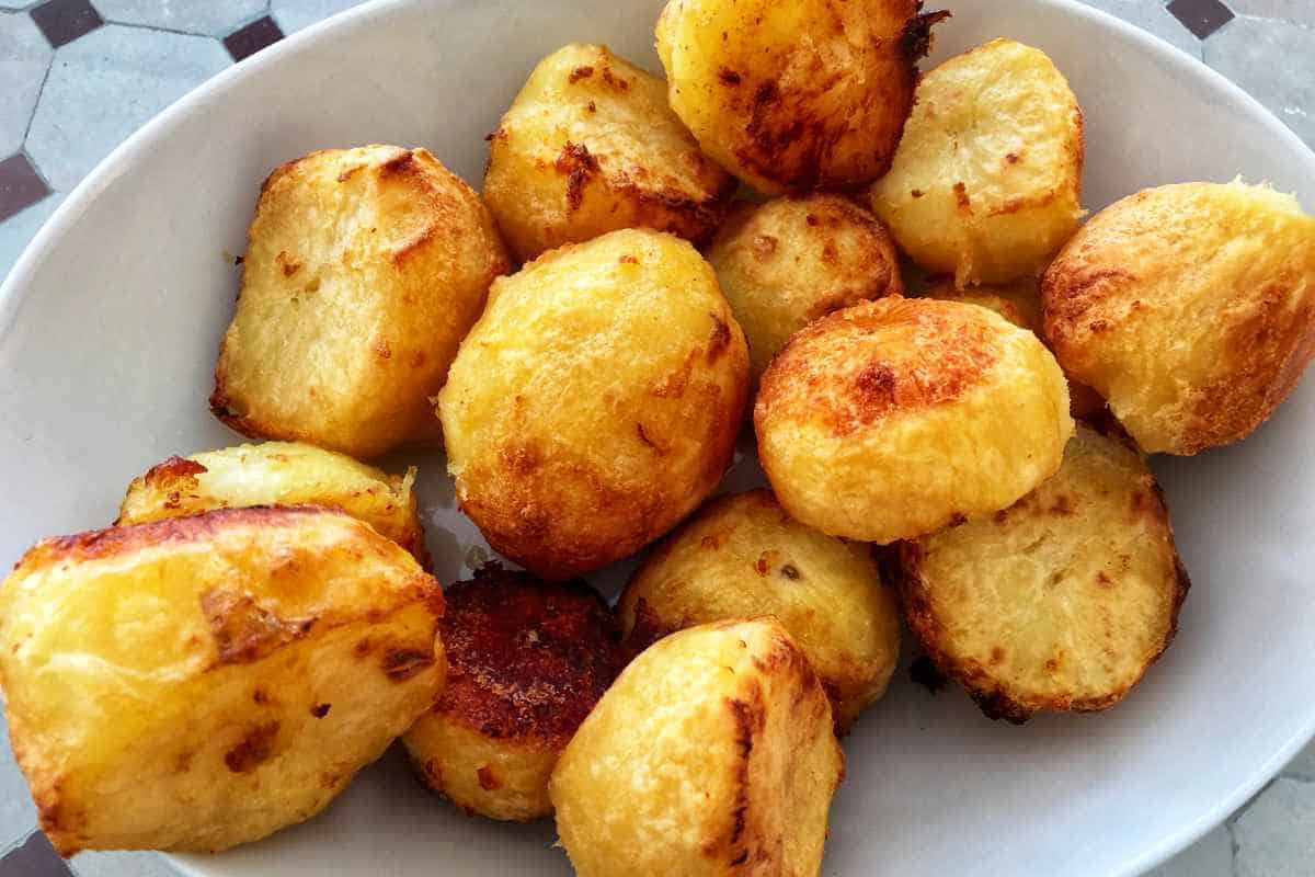 A white bowl filled with crispy, golden-brown roasted potatoes, arranged closely together on a tiled surface.