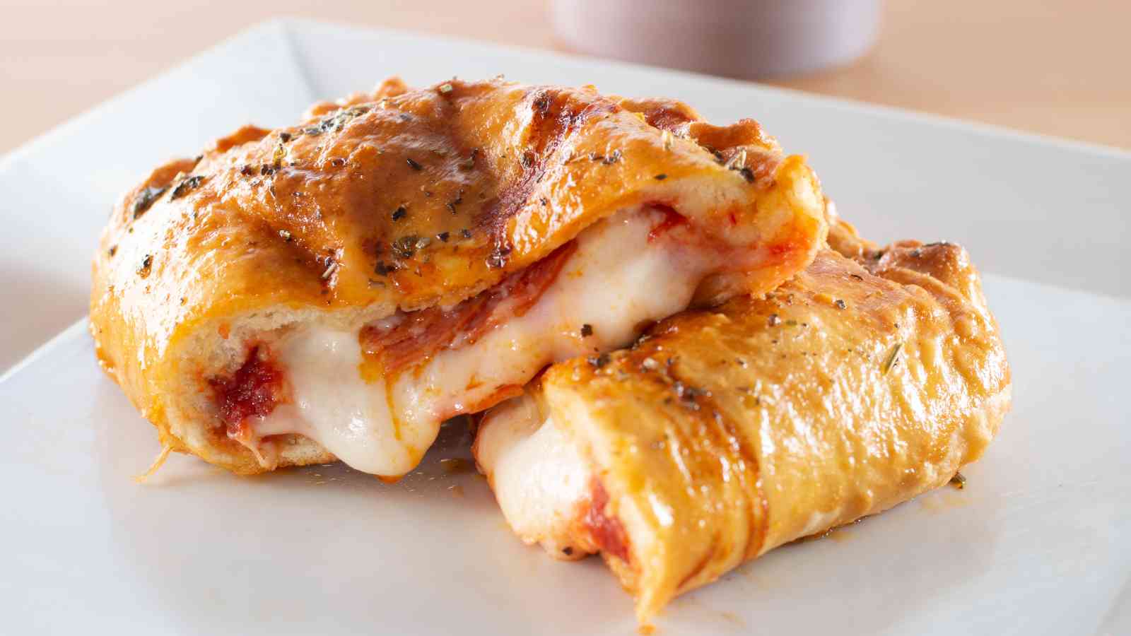 A close-up of a hot pockets cut in half, showing melted cheese, tomato sauce, and herbs inside a golden-brown crust on a white plate.