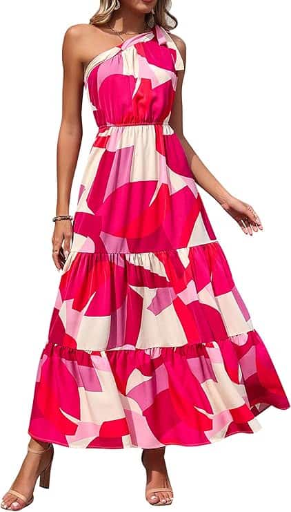 Woman wearing a sleeveless, one-shoulder maxi dress with pink, red, and white abstract patterns and tiered skirt, paired with heeled sandals.