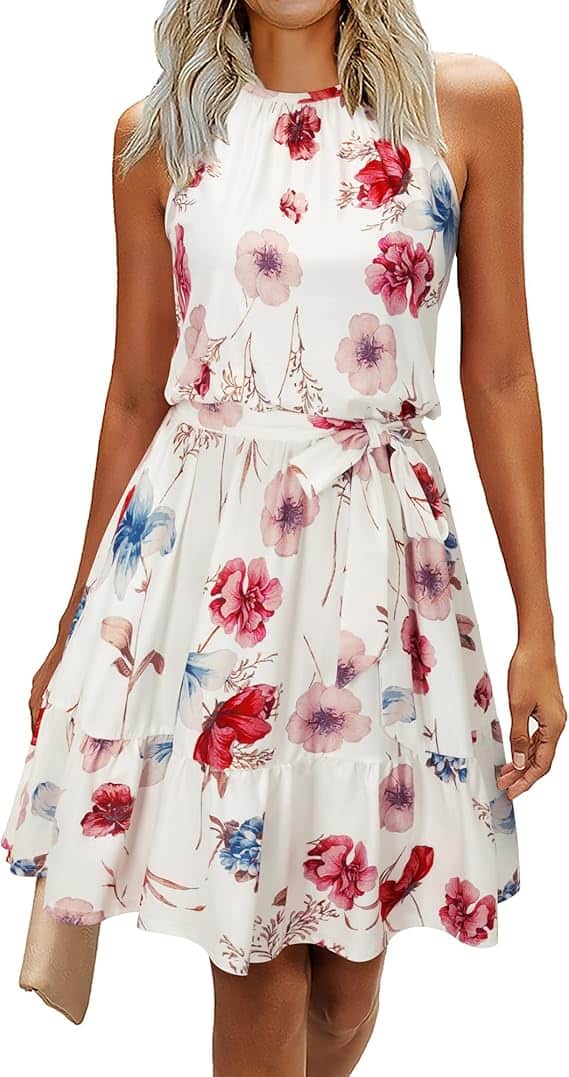 Woman wearing a sleeveless, knee-length white dress with a pink, red, and blue floral print pattern and a gathered waist.