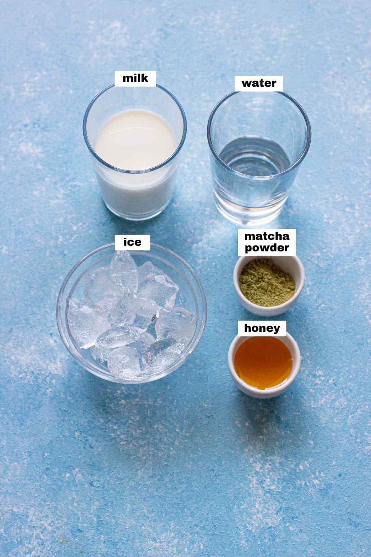 Five labeled ingredients—milk, water, ice, matcha powder, and honey—are arranged in separate glasses and bowls on a blue textured surface.