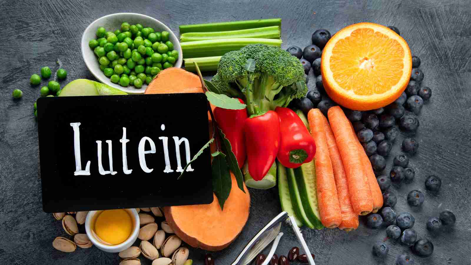 A variety of lutein-rich foods, including fruits, vegetables, and nuts, are arranged around a small chalkboard with the word "Lutein" written on it.