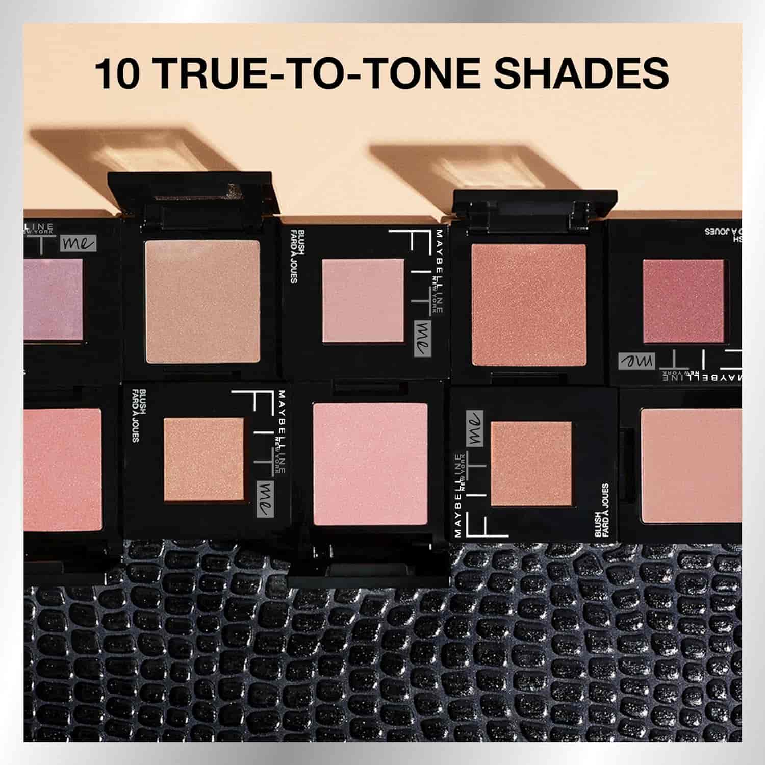 A display of eight Maybelline Fit Me blush compacts, open to show various pink and peach shades, under the text "10 TRUE-TO-TONE SHADES" on a textured surface.