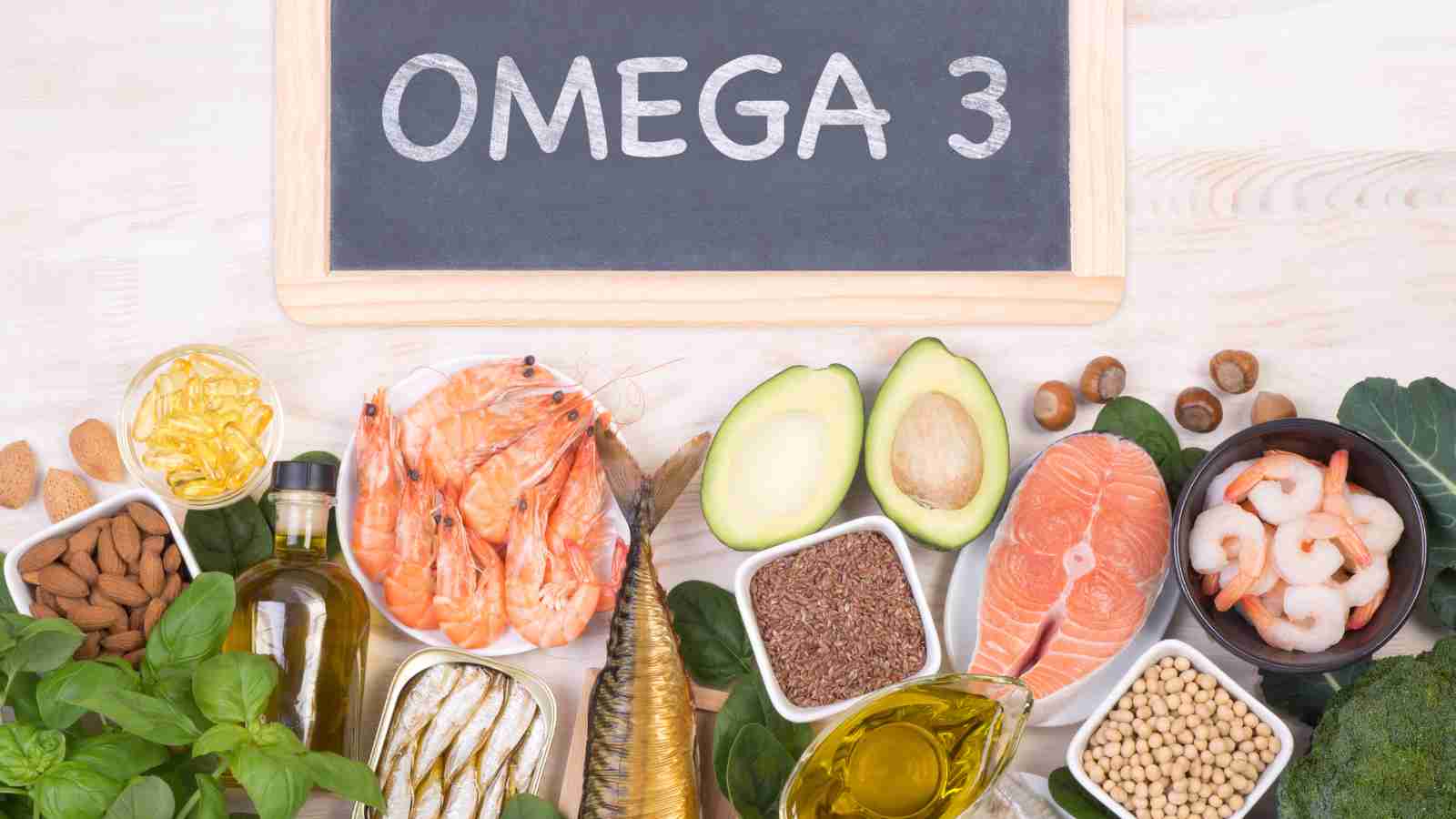 A variety of omega-3 rich foods, including fish, seafood, nuts, seeds, and oils, are arranged around a chalkboard that reads "OMEGA 3".