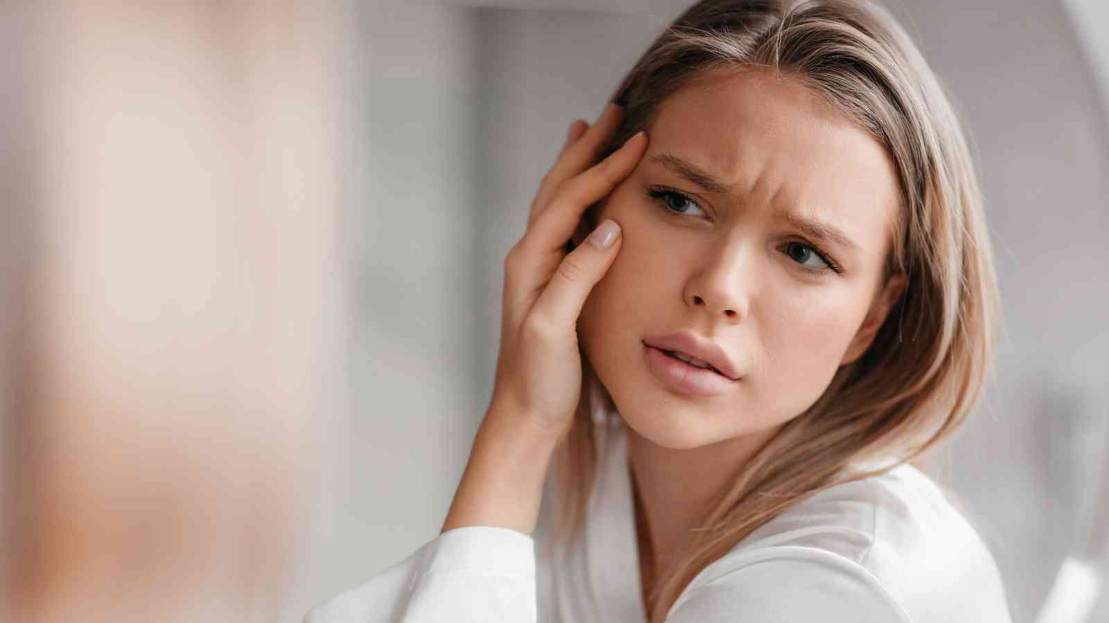 A woman with light hair rests her head on her hand and looks forward with a concerned or worried expression.