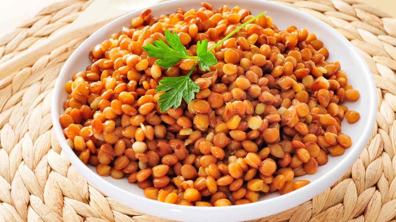 A white bowl filled with cooked brown lentils, garnished with fresh parsley, placed on a woven mat.
