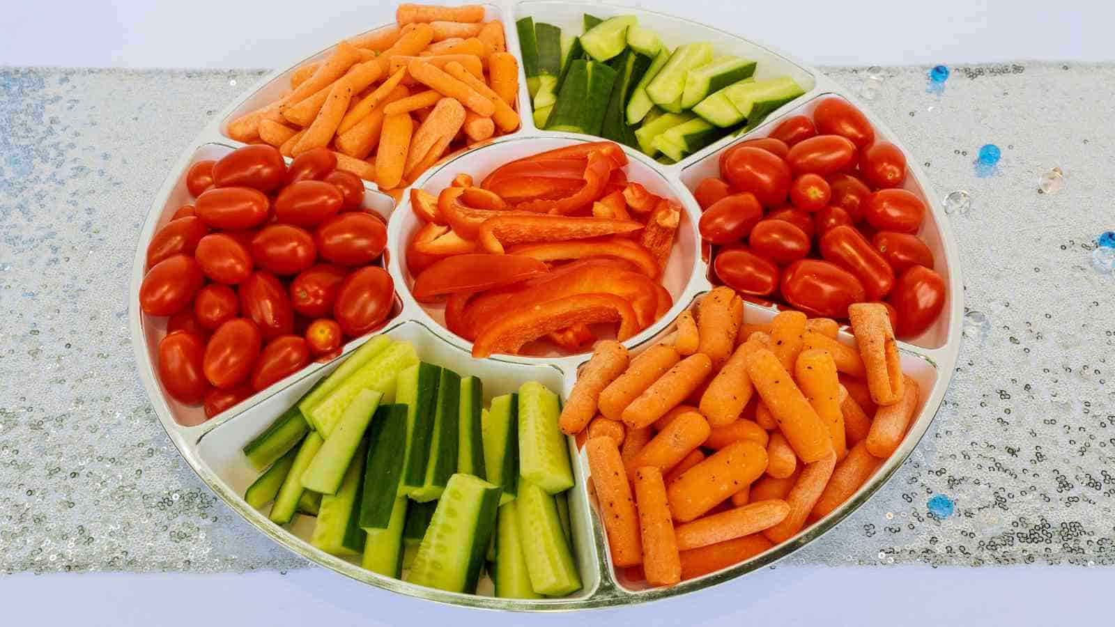 A divided tray with sections of grape tomatoes, baby carrots, cucumber sticks, and sliced red bell peppers arranged neatly.