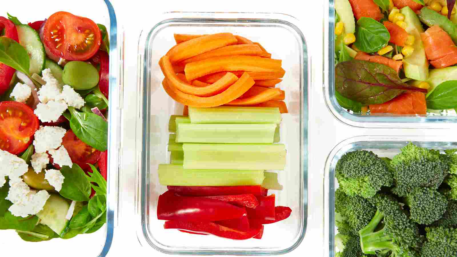 Three glass containers with fresh salad, sliced vegetables (carrots, celery, red pepper), and broccoli, viewed from above on a white background.