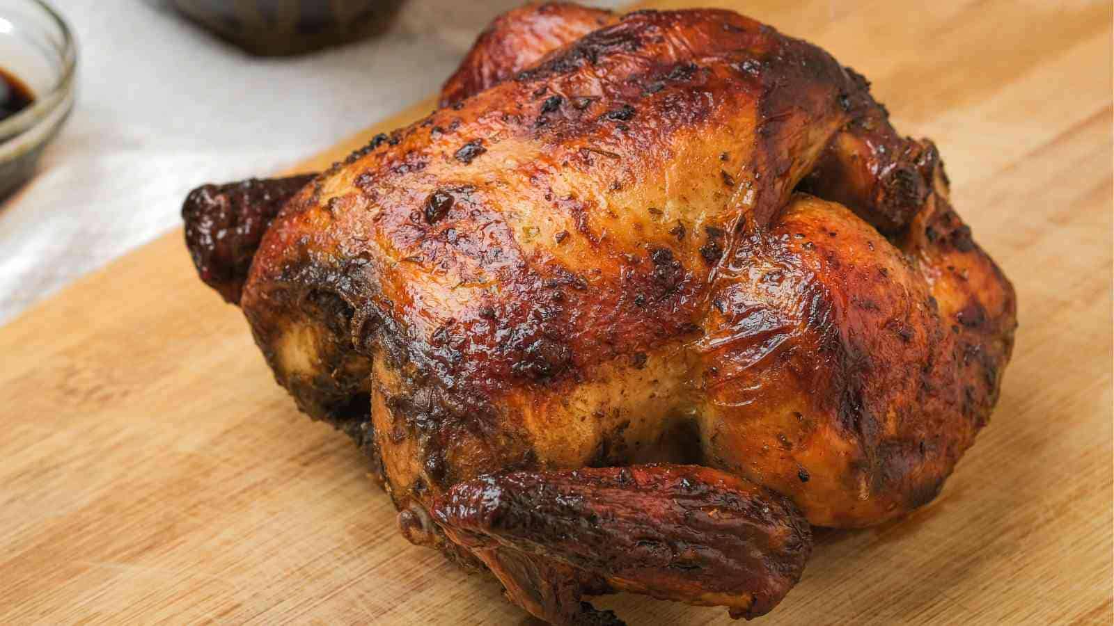 A whole roasted chicken with crispy, golden-brown skin sits on a wooden cutting board.