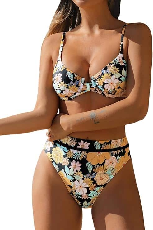 Woman wearing a high-waisted bikini with a black base and multicolored floral print, standing with arms crossed over her waist.