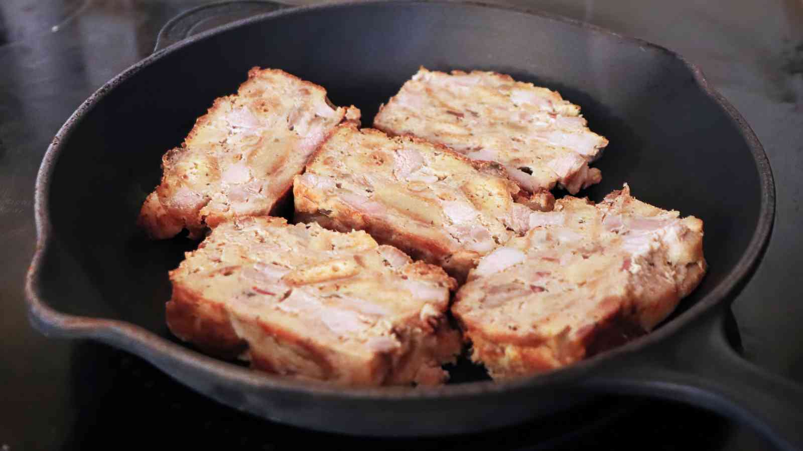 Five slices of scrapple are arranged and cooked in a black cast iron skillet.
