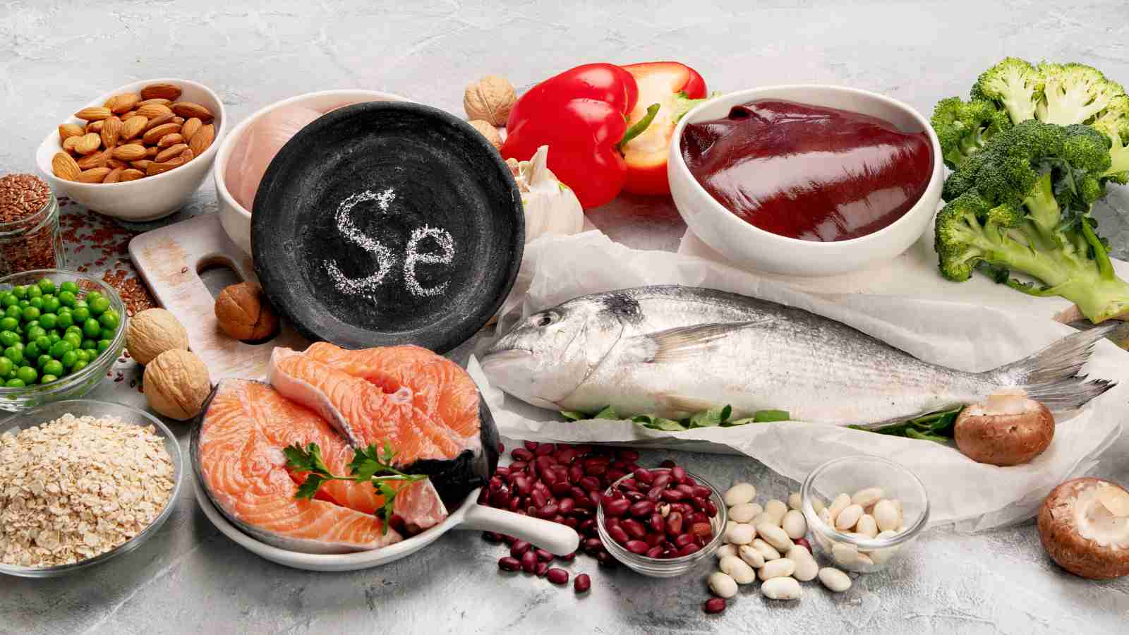 An assortment of selenium-rich foods, including fish, meat, nuts, grains, and vegetables, are arranged around a small chalkboard with the chemical symbol for selenium.