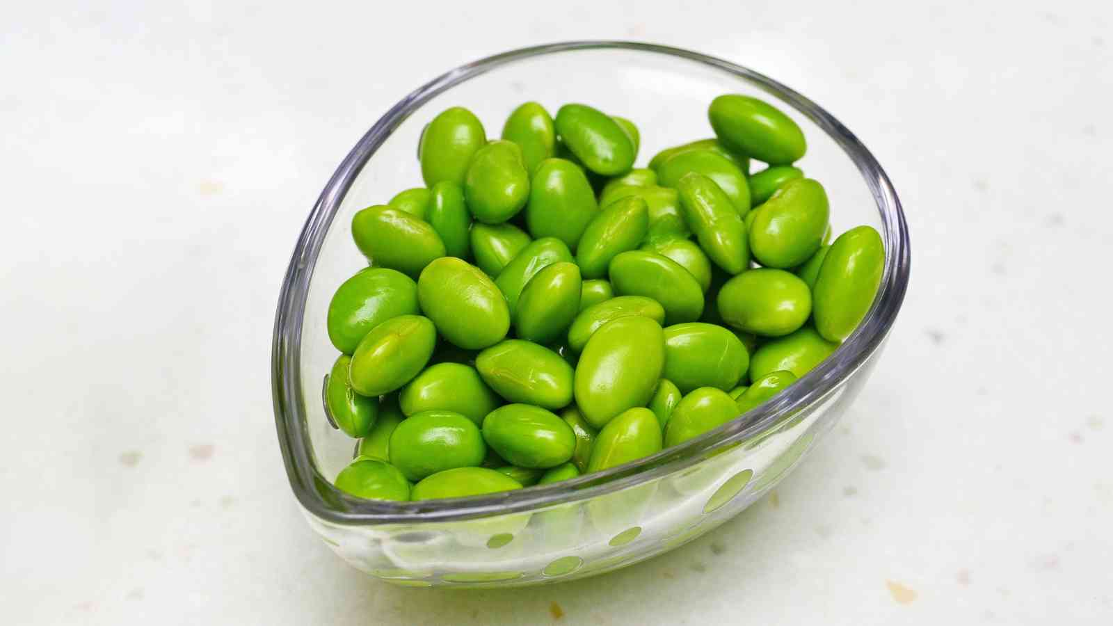 A small glass bowl filled with bright green edamame beans on a light-colored surface.
