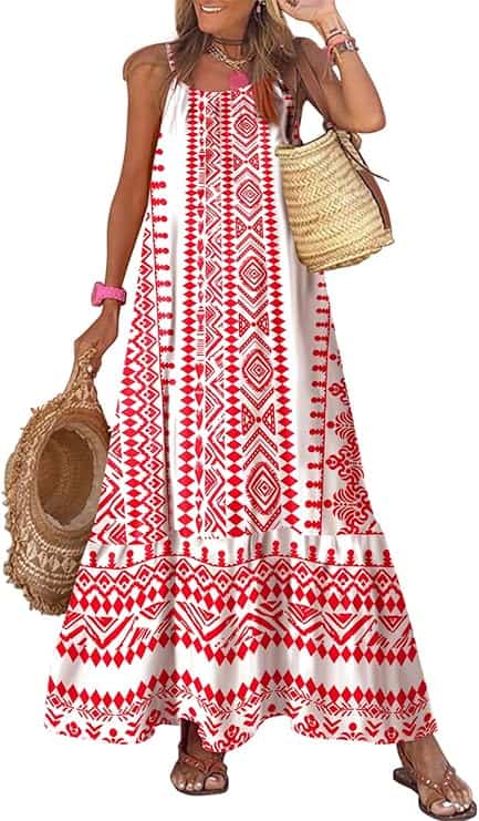 Woman wearing a sleeveless, long white dress with red geometric patterns, holding a straw hat and a woven bag, accessorized with bracelets and sandals.