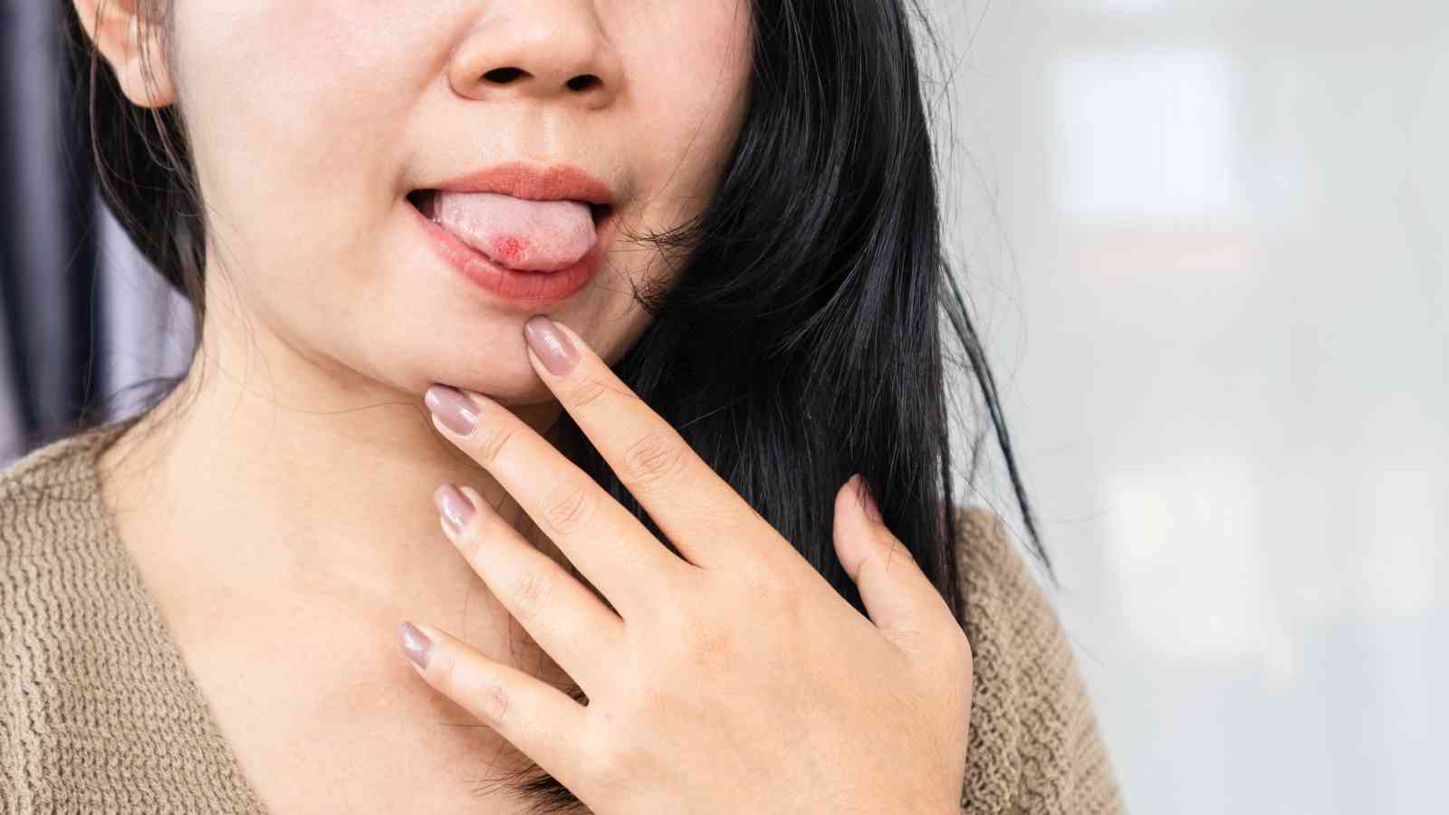 A woman touches her chin with her fingers while sticking out her tongue to one side.