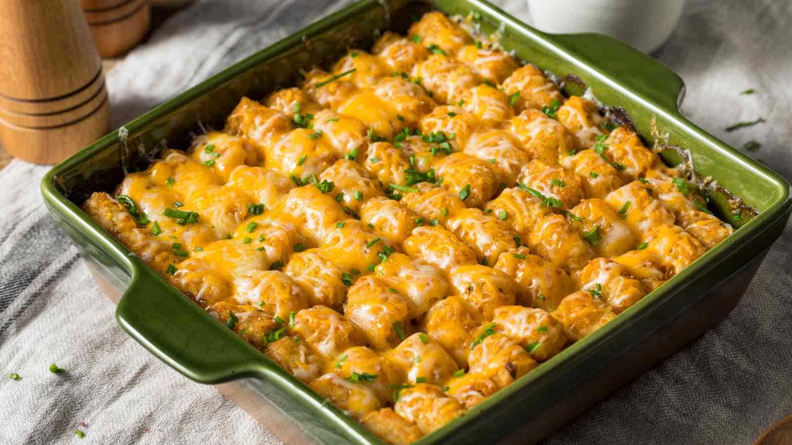 A baked tater tot casserole in a green square dish, topped with melted cheese and garnished with chopped herbs.