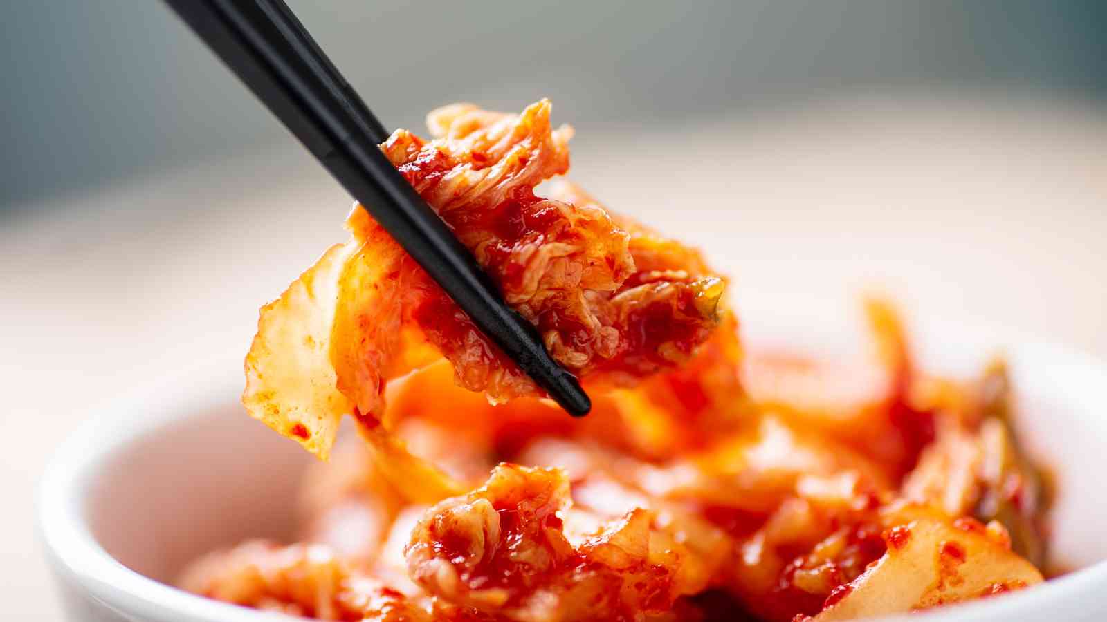 Chopsticks holding a portion of kimchi above a bowl filled with more kimchi.