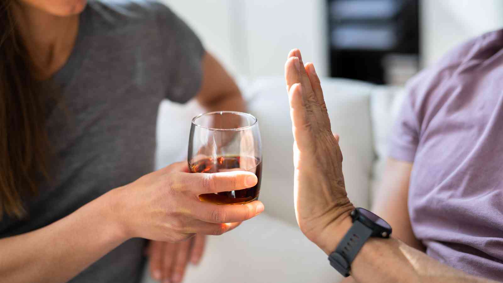 A person offers a glass of alcohol while another person raises their hand to refuse it.