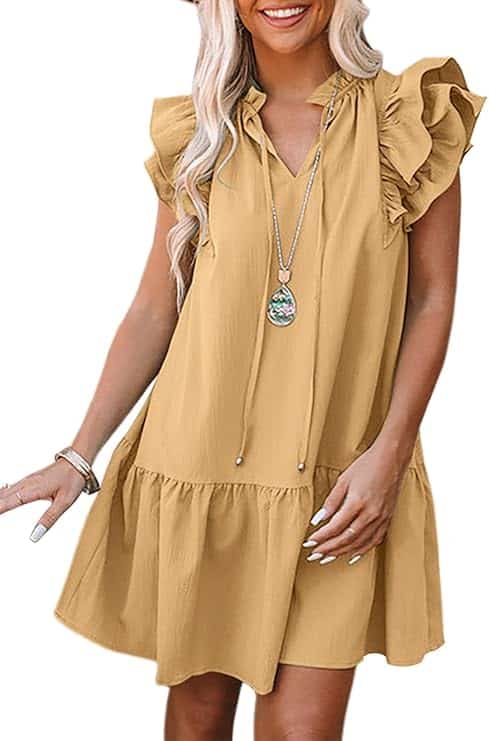 A woman wears a short, loose-fitting yellow dress with ruffled sleeves and a v-neck, accessorized with a long pendant necklace and bracelets.