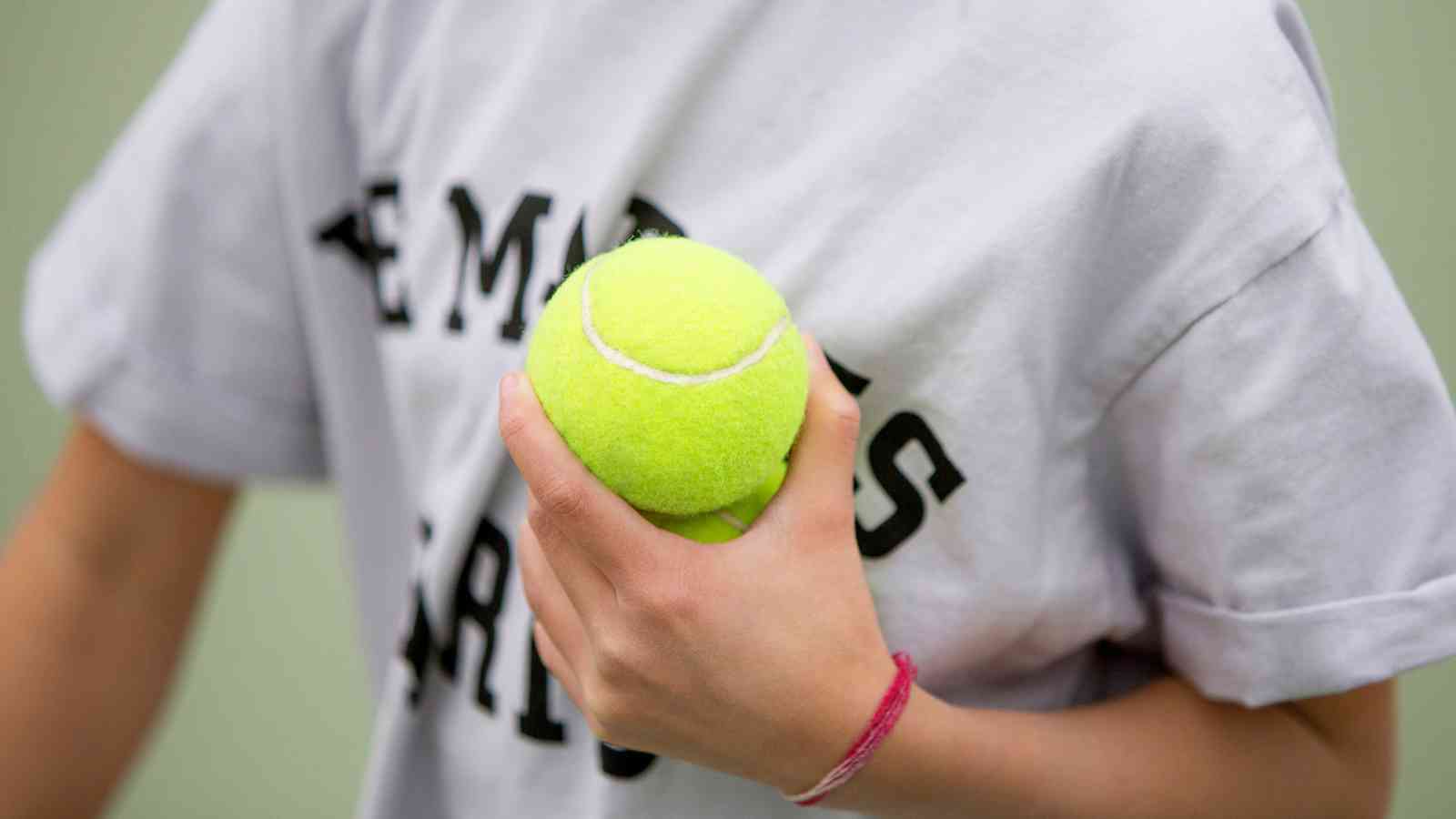 A person wearing a white shirt holds a yellow tennis ball in their right hand.