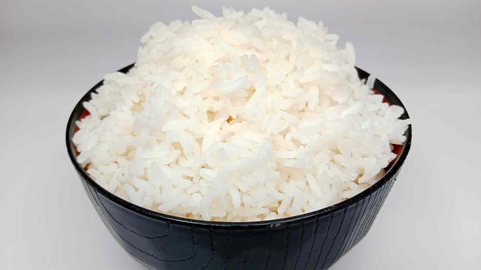 A black bowl filled with cooked white rice against a plain white background.