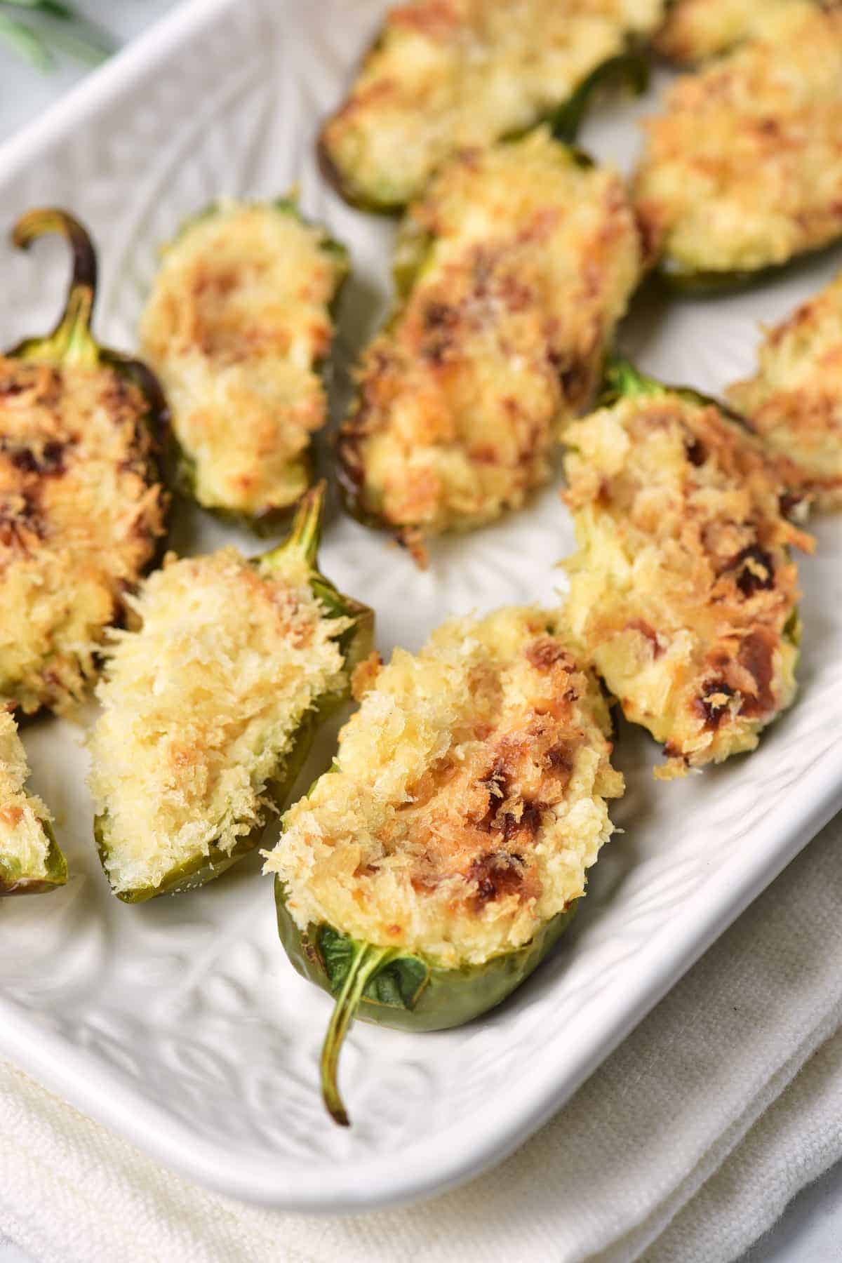 A white plate with several baked jalapeño poppers, each halved and filled with a golden-brown breadcrumb and cheese topping.