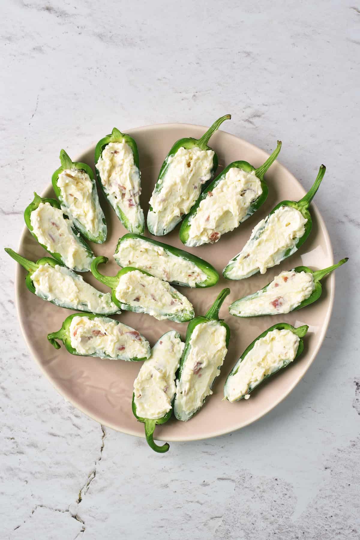 A plate of halved jalapeños filled with a creamy cheese mixture, arranged in a circular pattern on a light-colored plate.