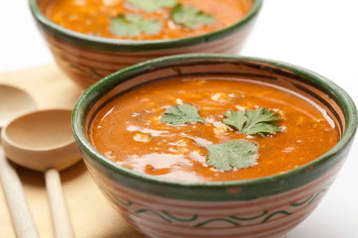 Two bowls of red soup garnished with cilantro, placed next to wooden spoons on a white surface.