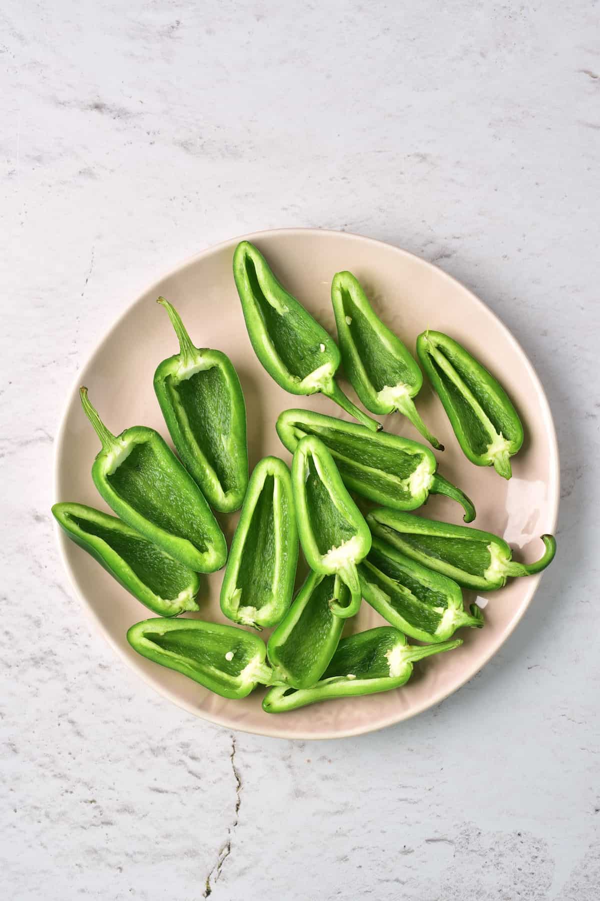 A beige plate with several green jalapeño peppers sliced in half lengthwise, placed on a light, textured surface.