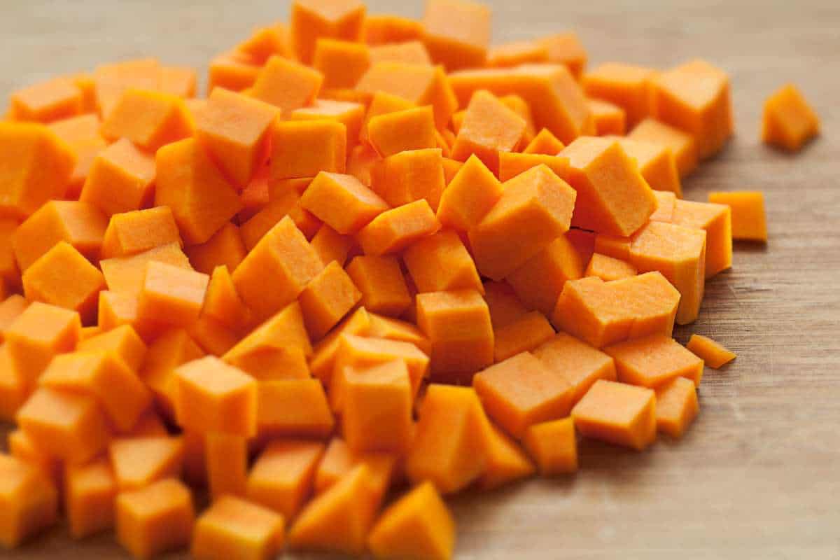 A pile of small, evenly diced butternut squash on a wooden cutting board.