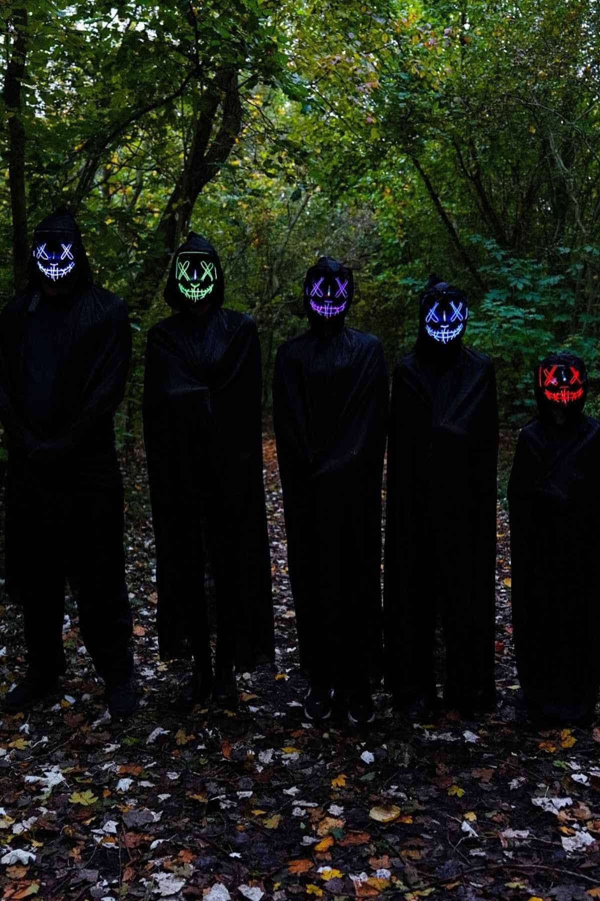 A family of five wearing all black costumes, standing straight in the woods.