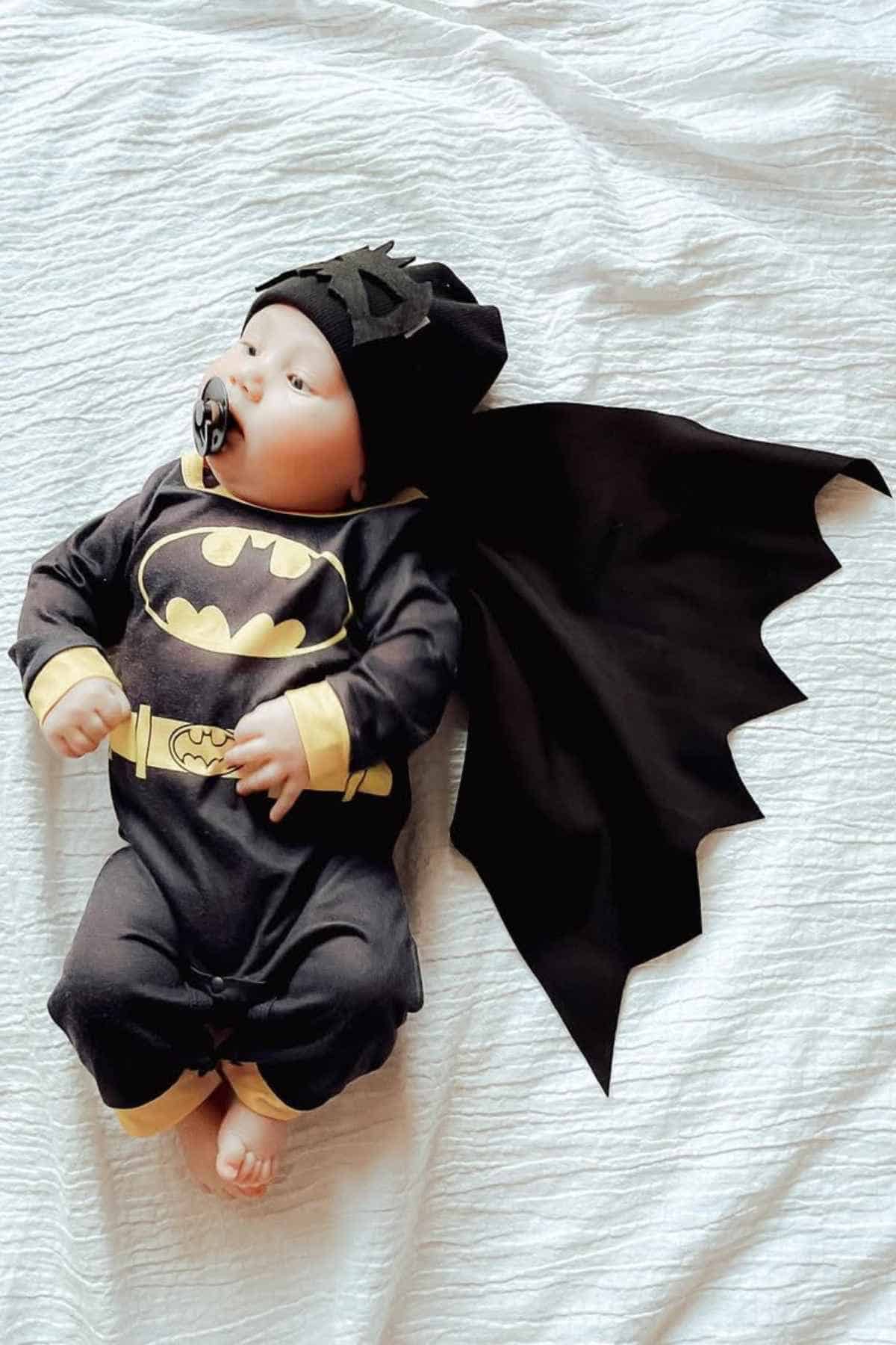 A baby dressed in a batman suit with wings, paired with a black pacifier on his mouth.