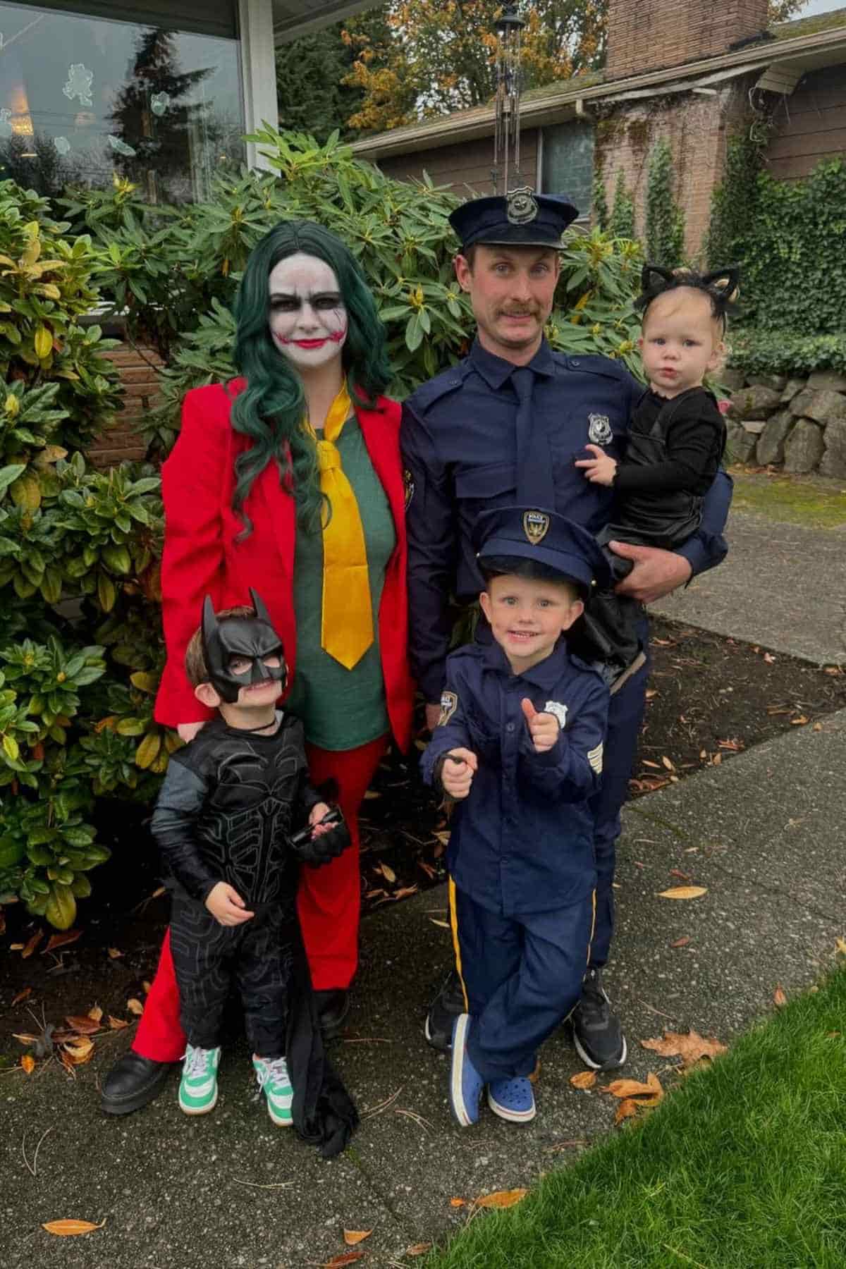 A family of five wearing different costumes. The Dad and son wears as a police officer, a little one wears as a batwoman, one kid as batman and Mom as Joker.