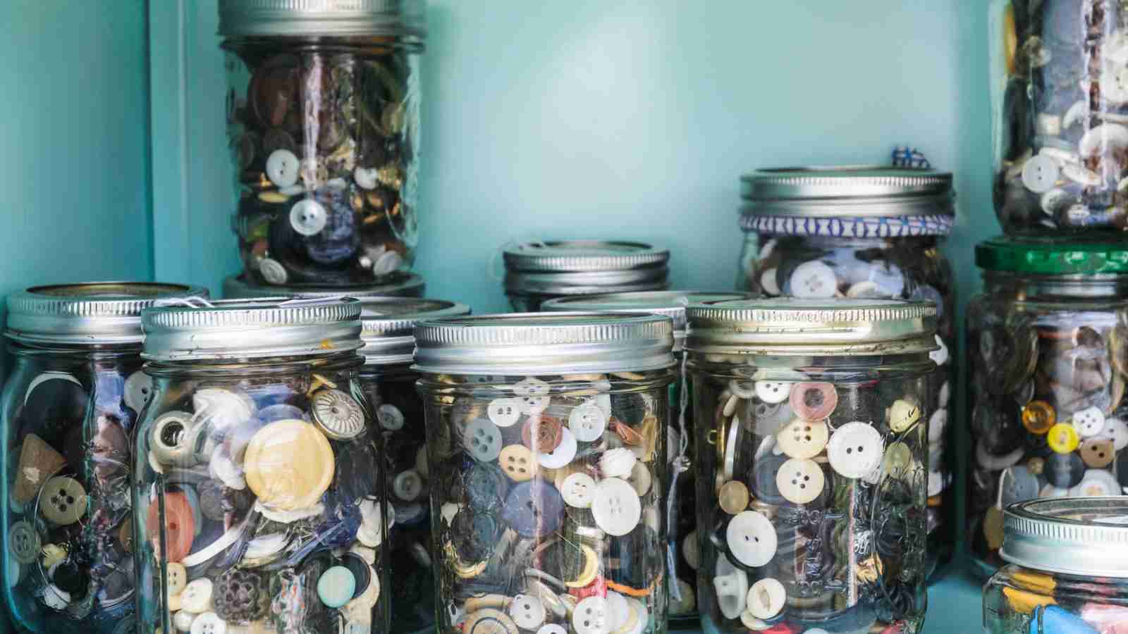 Several mason jars filled with various buttons are arranged on a shelf.