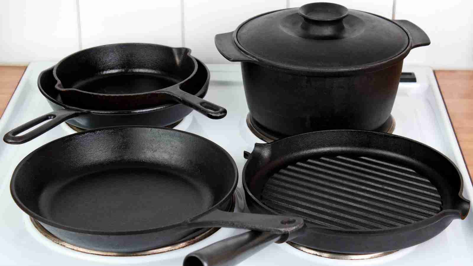 Four pieces of black cast iron cookware sit on a white stovetop.